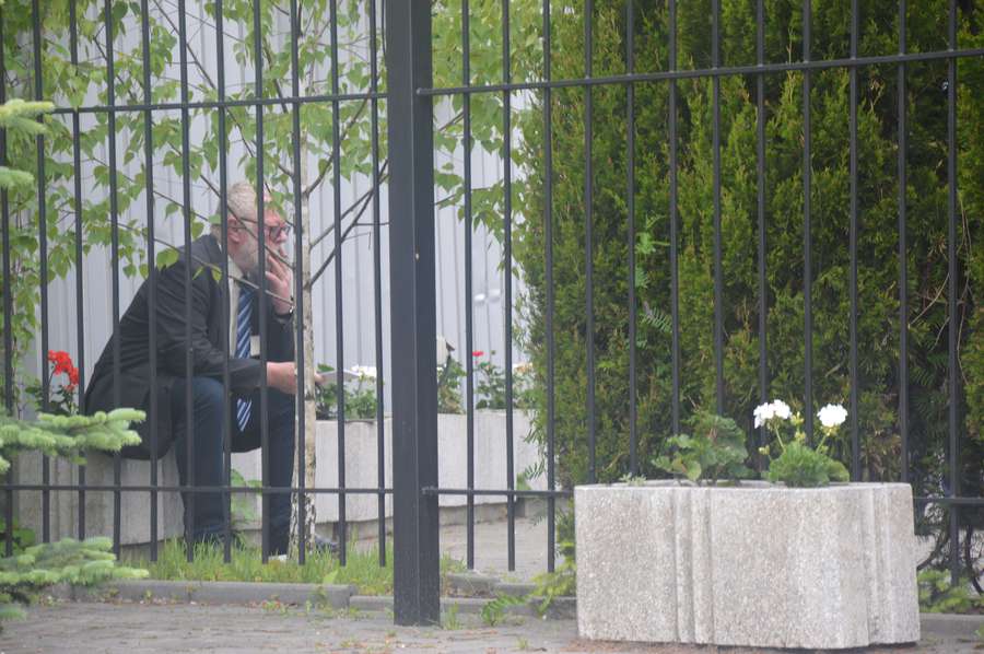 Кшиштоф Савіці неподалік від активістів, за парканом, щось конспектує і курить цигарку